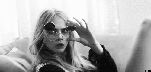 A GIF of Cara Delevigne lying back and putting on sunglasses